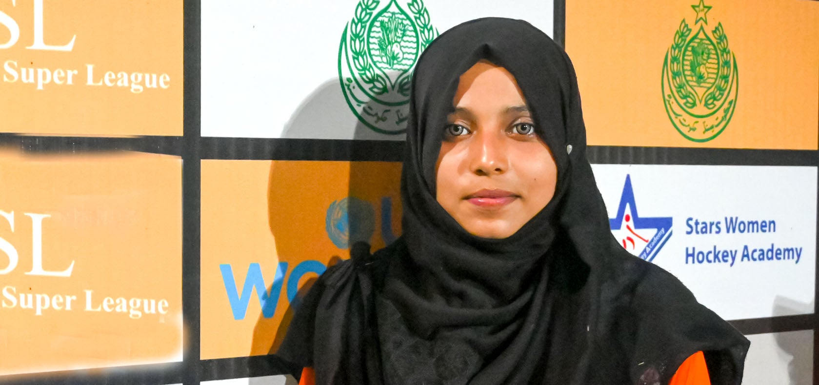 A young woman in her sportswear stands in front of the UN Women banner with her sports attire